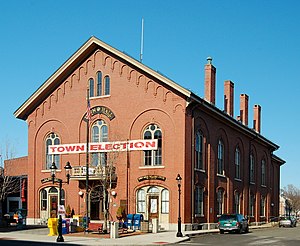 Picture of a long two-story brick building with four chimneys and a banner on it reading "Town election".